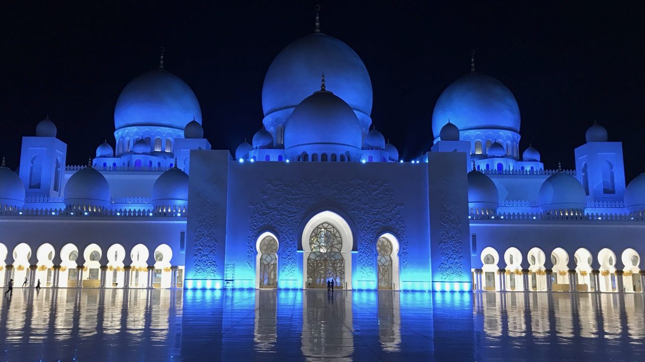 Scheich-Zayid-Moschee Abu Dhabi bei Nacht. Blau leuchtet die Mosche und glänzt vor dem dunklen Himmel besonders schön. Der Marmorboden sieht dabei aus wie ein endloses Meer.